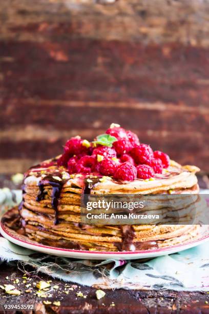 stack of wheat golden pancakes or pancake cake with freshly picked raspberry, chopped pistachios, chocolate sauce on a dessert plate, selective focus - raspberry sauce stock pictures, royalty-free photos & images