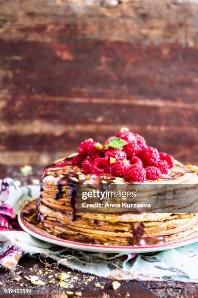 stack of wheat golden pancakes or pancake cake with freshly picked raspberry, chopped pistachios, chocolate sauce on a dessert plate, selective focus - raspberry sauce stock pictures, royalty-free photos & images