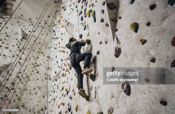 vista ad angolo basso dell'uomo atletico che si arrampica sul muro in una palestra. - scalata foto e immagini stock