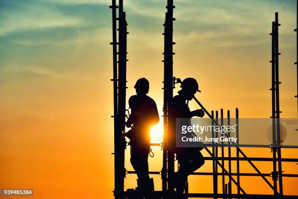 silhouette civil site engineer and construction worker working on scaffolding in industrial construction during sunset sky background over time job - baustelle gerüst sonne stock-fotos und bilder
