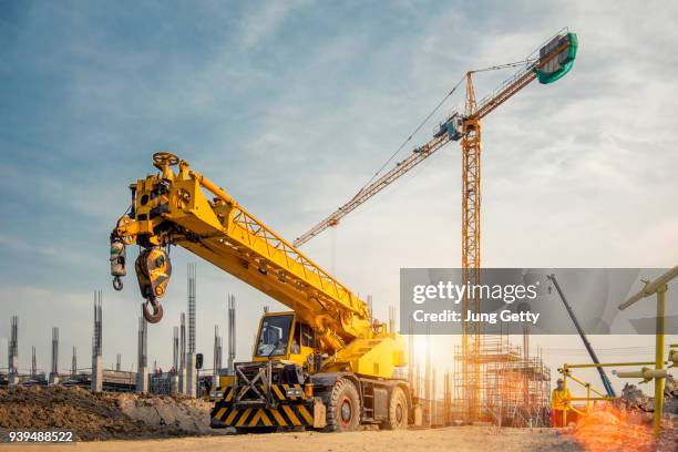 mobile crane on a road and tower crane in construction site - crane photos et images de collection