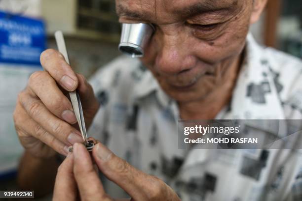 Chuan Kee uses a magnifying eyepiece as he inspects a customer's wrist watch in Bentong, outside Kuala Lumpur in nearby Pahang state on March 29,...