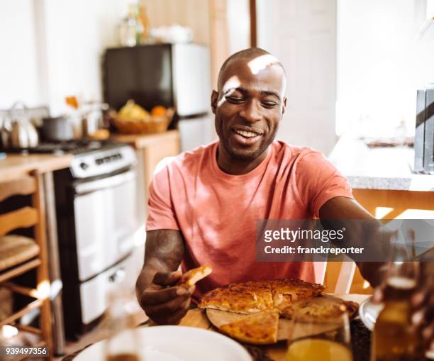 man eating a pizza in the kitchen - black man eating stock pictures, royalty-free photos & images