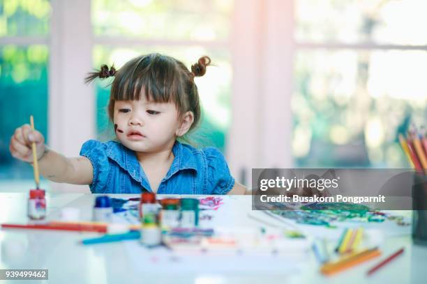 little girl painting with paintbrush and colorful paints on desk background - toddler drawing stock-fotos und bilder