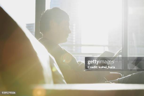 man reading a book on sofa - twilight book stock pictures, royalty-free photos & images