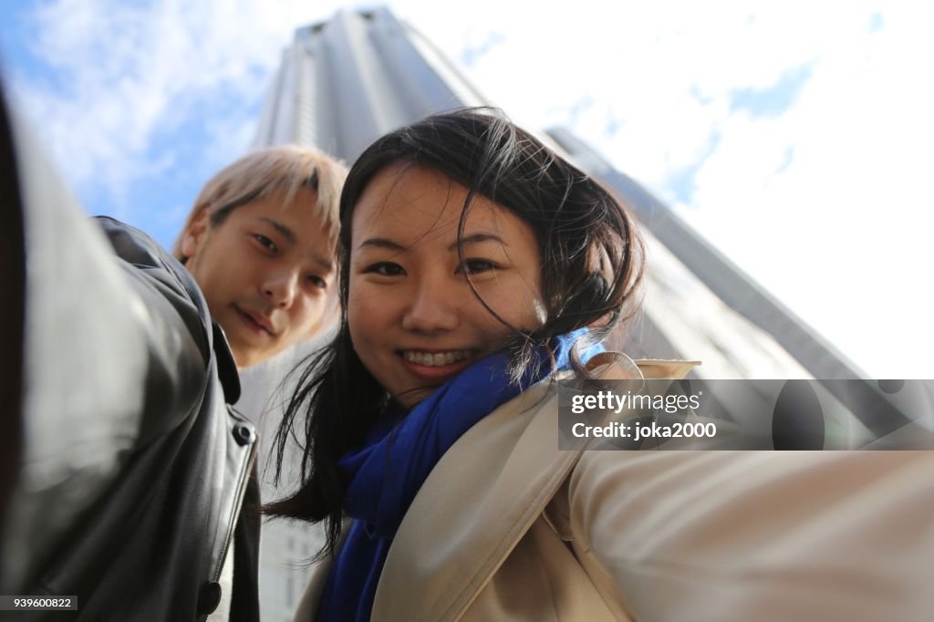 若い男と女の背の高いビルの前で selfies を撮影