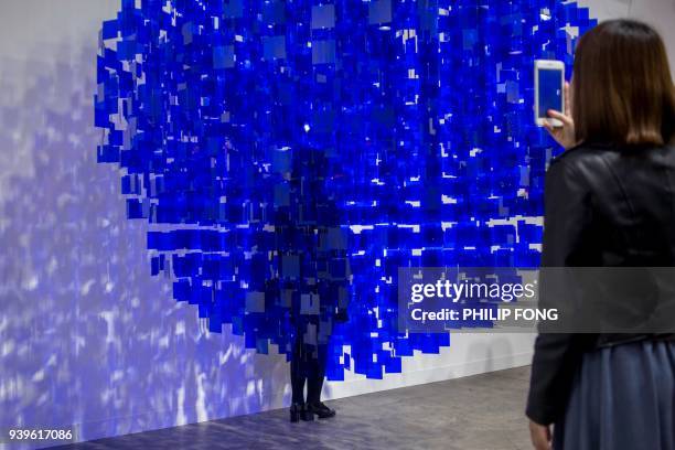 Woman poses for a photograph behind artist Julio Le Parc's "Sphère bleue" at Art Basel in Hong Kong on March 29, 2018. / AFP PHOTO / Philip FONG /...