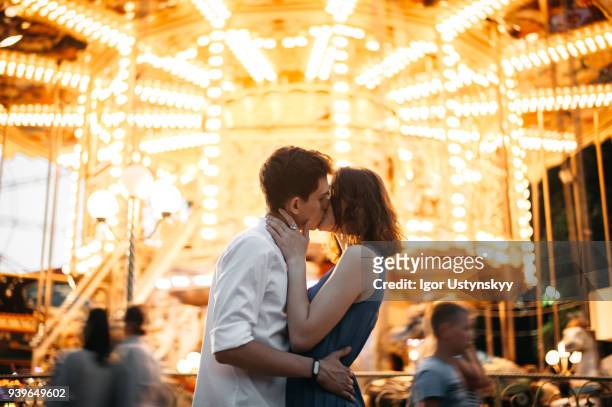 couple kissing near the marry-go-round in the park - der kuss stock-fotos und bilder