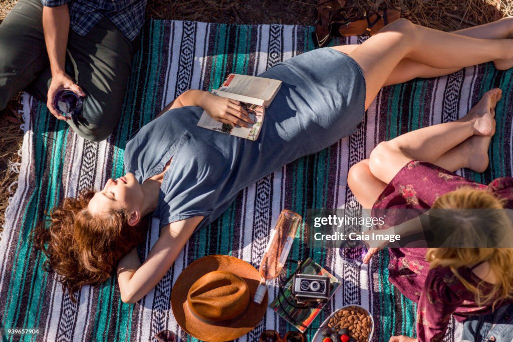 Overhead view young woman with book relaxing on picnic blanket