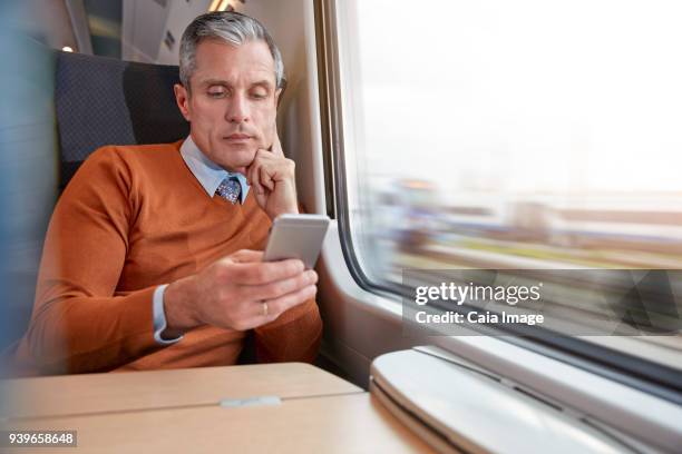 focused businessman using smart phone at passenger train window - train interior stock pictures, royalty-free photos & images