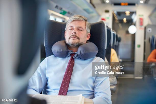 tired businessman with neck pillow sleeping on passenger train - train interior stock pictures, royalty-free photos & images