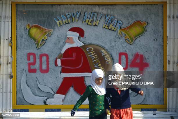 Two Iraqi girls cross a street in Baghdad in front of a Seasonal Greeting sign 31 December 2003. Iraqi Police have taken strict security measures...