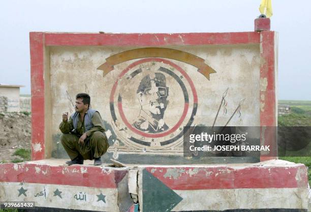 An Iraqi Kurdish peshmerga volunteer fighter of the Kurdistan Democratic Party smokes a cigarette 06 April 2003 in front of a painting of Iraqi...