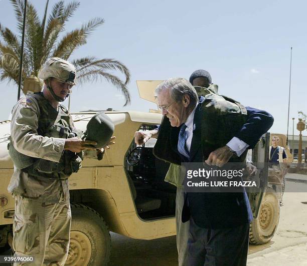 Secretary of Defense Donald Rumsfeld puts on a bullet-proof flack jacket 30 April 2003 upon his departure from Saddam Hussein's Abu Gharyb Palace in...