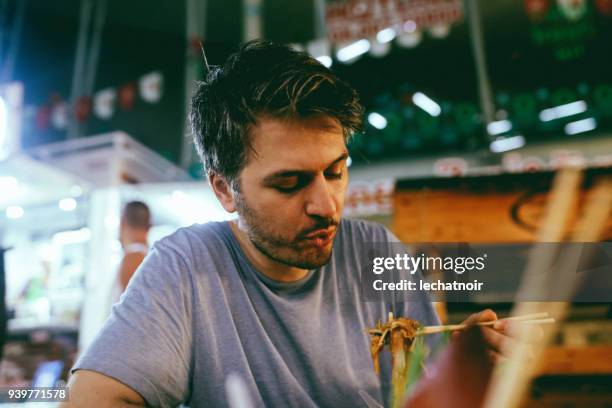 junger mann essen authentische thai-küche auf einem straßenmarkt in bangkok, thailand - thai ethnicity stock-fotos und bilder
