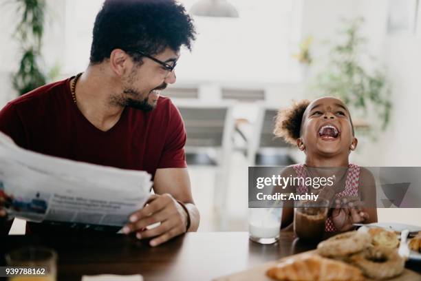 little girl bursts into laugh while having breakfast with her father - newspaper on table stock pictures, royalty-free photos & images