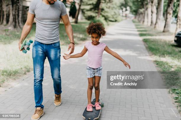 lächelndes kind stehend auf longboard während ihres vaters hand hält - father longboard stock-fotos und bilder