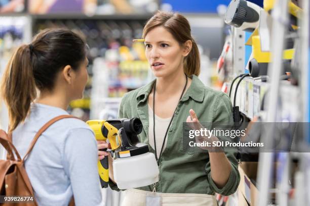hardware store employee discusses paint sprayer with customer - backpack sprayer stock pictures, royalty-free photos & images