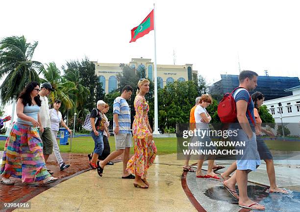 In this picture taken on November 12 foreign tourists walk past The Maldivian National Flag in a pedestrianised area of Male. The IMF has approved a...