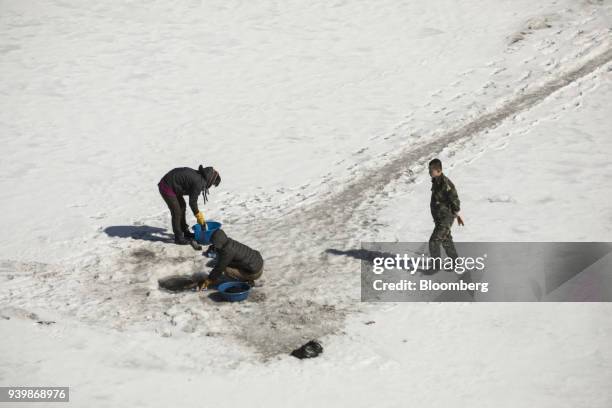 Soldier looks on as women wash clothes through a hole broken in the frozen Yalu River in Hyesan, North Korea, seen from across the border in...