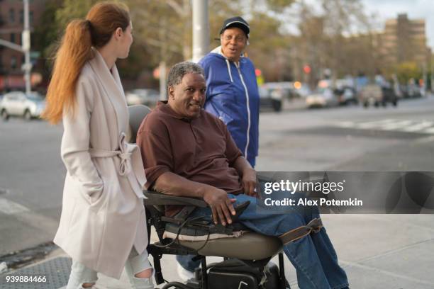 the white teenager girl talking with disabled wheel-chaired african american man and woman when they walking on the street together - bronx street stock pictures, royalty-free photos & images