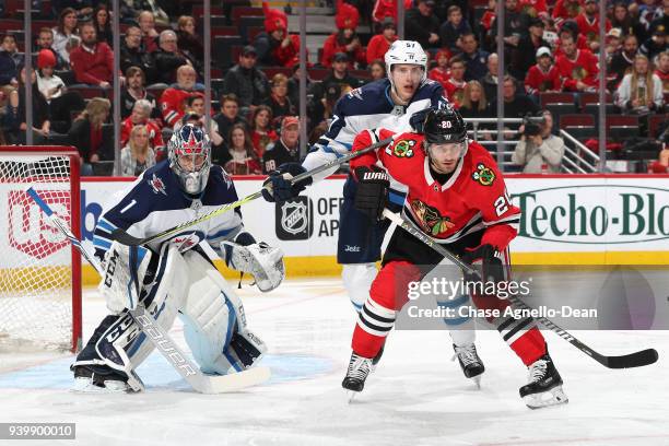 Tyler Myers of the Winnipeg Jets and Brandon Saad of the Chicago Blackhawks wait in position in front of goalie Eric Comrie in the second period at...