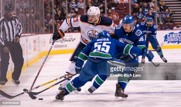 Leon Draisaitl of the Edmonton Oilers tries to get past Alex Biega of the Vancouver Canucks and Jussi Jokinen in NHL action on March 29, 2018 at...