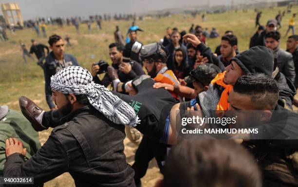 Picture taken on March 30, 2018 shows an injured Palestinian youth being carried by other protesters as they flee during clashes after a...