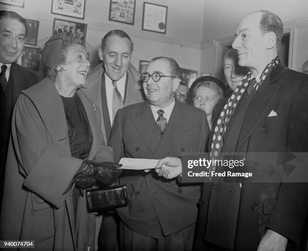 Actress Cicely Courtneidge hands over a cheque for £16 the amount raised at a recent Ivor Novello Memorial Performance, to actor John Gielgud at the...
