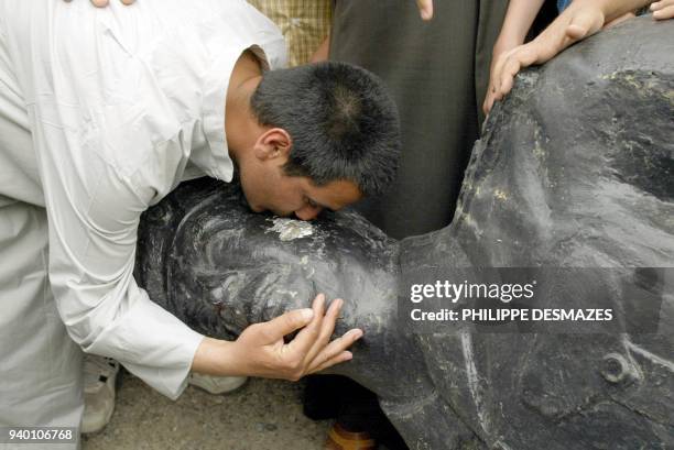 Resident of Tikrit, the hometown of toppled Iraqi president Saddam Hussein, kisses a fallen bronze statue of the leader 19 April, 2003. US soldiers...