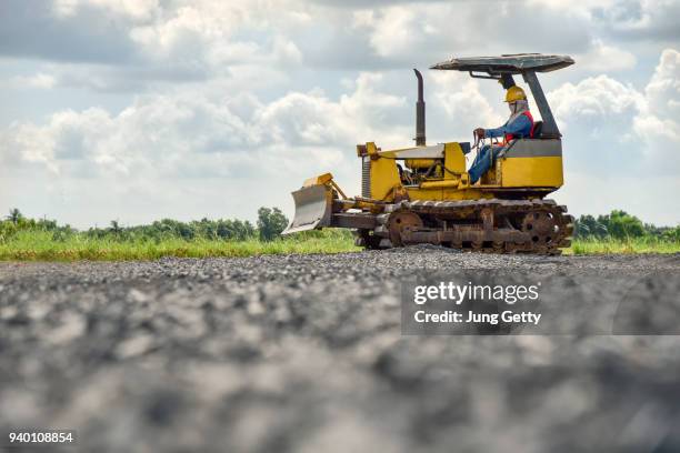 construction worker in safety uniform driving grader tractor or construction machine move the soil in construction site and beautiful sky background - pressmaschine stock-fotos und bilder