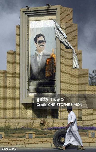 An Iraqi civilian rolls a stolen tire past a burning portrait of Iraqi President Saddam Hussein in Baghdad 10 April 2003, one day after the collapse...