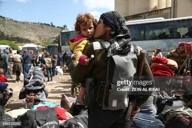 Rebel fighter from Eastern Ghouta, holds his weapon as he kisses a child after arriving in Qalaat al-Madiq, some 45 kilometres northwest of the...