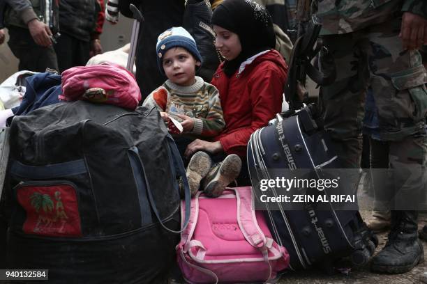 Syrian children evacuated from Eastern Ghouta sit on luggage after arriving in Qalaat al-Madiq, some 45 kilometres northwest of the central city of...