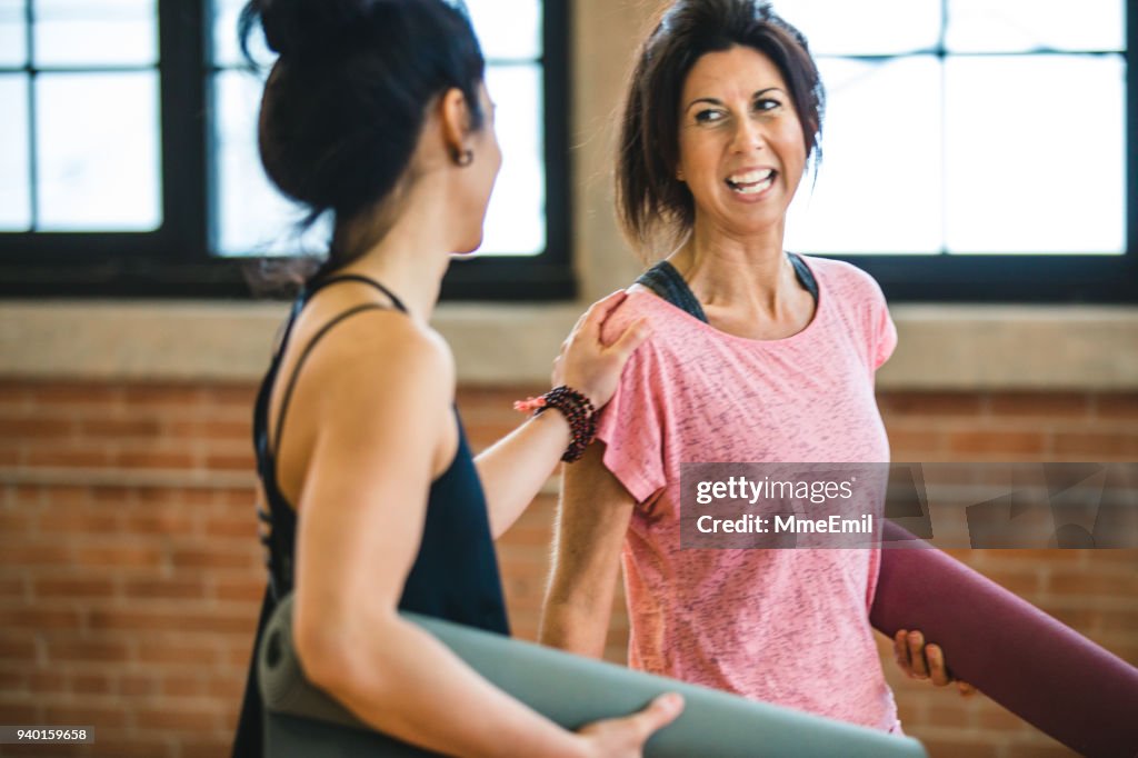 Two women talking and laughing. Yoga training class preparation