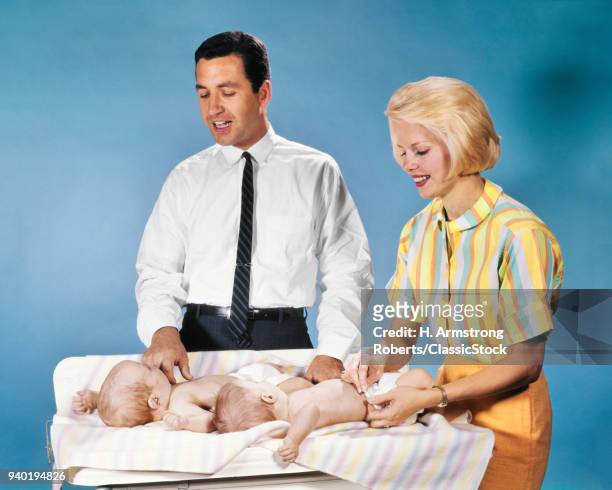 1960s MOTHER AND FATHER DIAPERING TWO TWIN BABIES CLOTH DIAPERS ON CHANGING TABLE