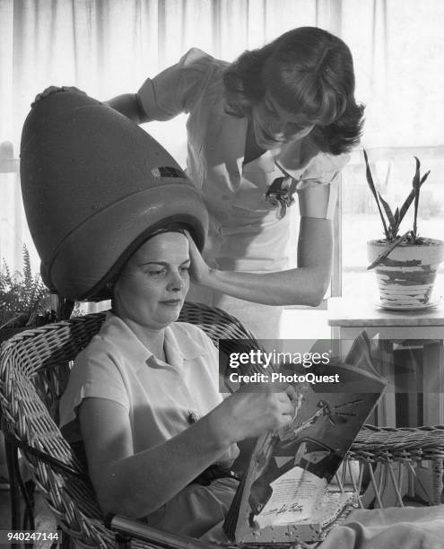 View of a hair stylist as she adjusts a hair dryer on a customer's head at a beauty parlor, Wilmington, Delaware, 1949.
