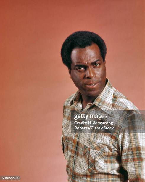 1970s AFRICAN AMERICAN MAN WEARING PLAID SHIRT LOOKING AT CAMERA WITH ANGRY MEAN QUESTIONING OR INQUISITIVE FACIAL EXPRESSION
