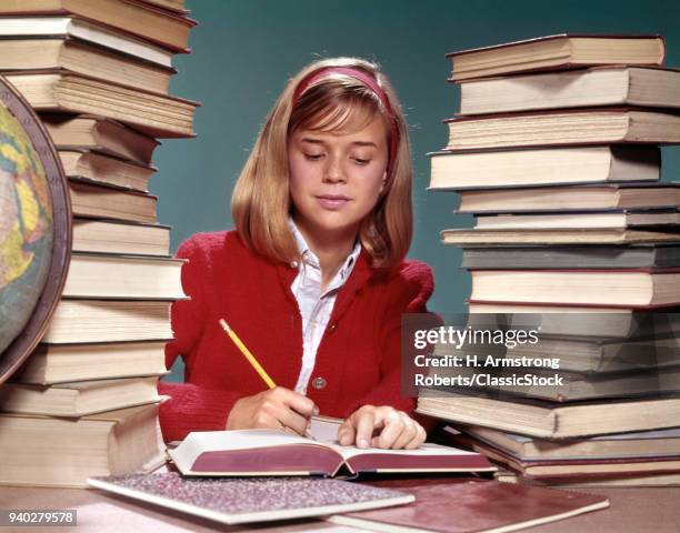 1960s TEENAGED GIRL WITH BOOKS STACKED ON BOTH SIDES OF HER AND GLOBE WRITING IN NOTEBOOK