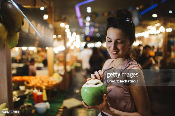 lächelnde junge frau, die eine leckere und frische kokosnuss-wasser unterwegs - food in market stock-fotos und bilder