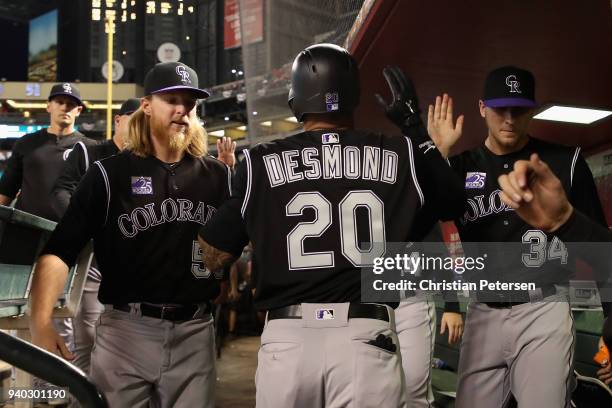 Ian Desmond of the Colorado Rockies high fives Jon Gray and Jeff Hoffman in the dugout after hitting a two-run home run against the Arizona...