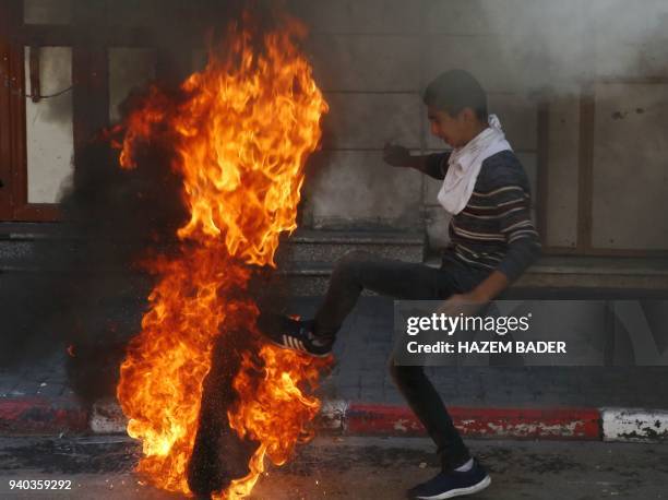 Palestinian demonstrator kicks a burning tire towards Israeli forces during clashes on March 31, 2018 in the occupied West Bank city of Hebron as a...