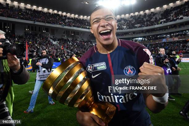 Paris Saint-Germain's French forward Kylian Mbappé holds the trophy as he celebrates after victory in the French League Cup final football match...