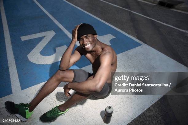 portrait of shirtless athlete sitting on all-weather running track and smiling, barcelona, spain - all weather running track fotografías e imágenes de stock