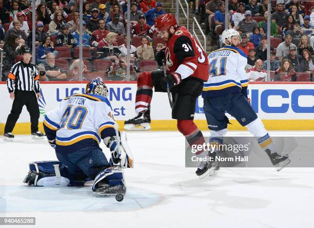 Goalie Carter Hutton of the St Louis Blues deflects the puck wide of the net with his skate as Zac Rinaldo of the Arizona Coyotes skates in past...