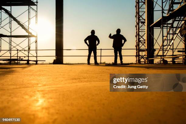 construction engineers supervising progress of construction project stand on new concrete floor top roof and crane background - building silhouette stock-fotos und bilder