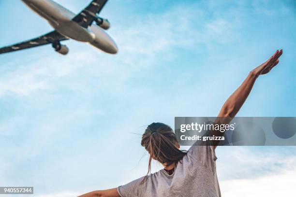 achteraanzicht van een jonge vrouw met uitgestrekte armen imiteren flying commerciële vliegtuig boven haar - commercial aircraft flying stockfoto's en -beelden