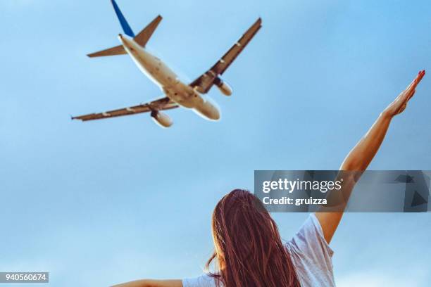 vista posteriore di una giovane donna con le braccia tese imitando aereo commerciale volante sopra di lei - one young woman only foto e immagini stock