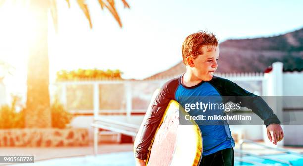 junge hält sich an surfbrett am pool - mikkelwilliam stock-fotos und bilder