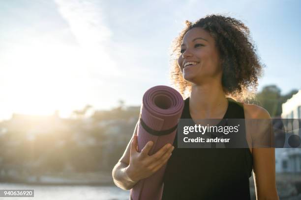 donna in forma che tiene in mano un tappetino da yoga in spiaggia - ginnastica foto e immagini stock